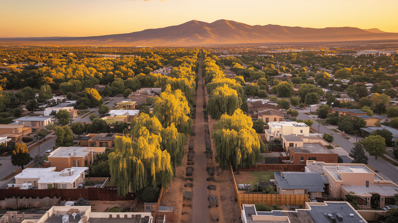 Aerial view of Albuquerque residential neighborhoods stretching toward the Sandia Mountains at golden hour, showing mature tree canopy in the North Valley and rooftop density in the Northeast Heights.