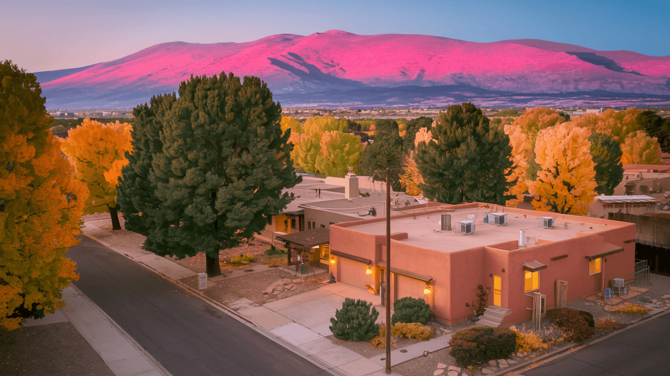 Aerial view of an Albuquerque neighborhood in fall with the Sandia Mountains glowing pink at dusk, adobe homes and mature cottonwood trees turning gold along a quiet residential street