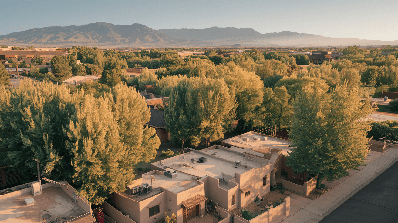Aerial view of an Albuquerque residential neighborhood in summer, with the Sandia Mountains visible in the background, adobe-style rooftops and mature cottonwood trees lining the streets below