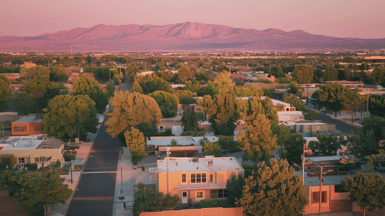 Aerial view of Albuquerque's Northeast Heights neighborhood at golden hour, with the Sandia Mountains glowing pink in the background and tree-lined residential streets below